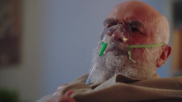 一位年老体衰的男子在家中独立治疗 用氧气面罩来舒缓呼吸 并把被单套在肩上保暖 一个病人患有结肠炎或支气管哮喘 — 图库视频影像