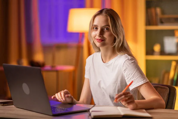 Śliczna Uśmiechnięta Blond Studentka Siedzi Przy Stole Mieszkaniu Używa Laptopa — Zdjęcie stockowe