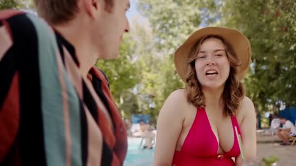 プールサイドで会話をする2人の幸せな人々のミッドショット 屋外プールでのフレンドリーなディスカッション ボーイフレンドは 夏に日光浴をするときにガールフレンドと話す 高品質の4K映像 — ストック動画