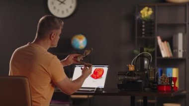 Grafik tasarımcısı, insan çene kemiğinin plastik 3D baskılı modelini tutuyor. Dizüstü bilgisayarın ön planında kırmızı renkli bir kalp resmi. Protezler için biyobasım organları konsepti ve