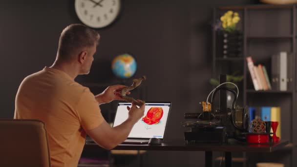 男性のグラフィックデザイナーは 人間の必須のプラスチック3Dプリントモデルを保持しています ラップトップ画面の前景に赤い色のハートのスケッチ 義肢のためのバイオプリンティング臓器の概念と — ストック動画