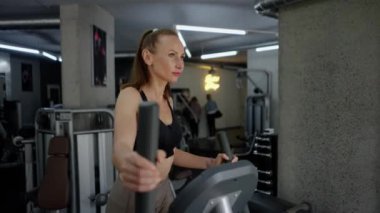 Mükemmel formda genç ve narin bir kadın spor salonuna girer ve bacak egzersizi makinesini özelleştirir. El hareketi ve pedal çevirme. Spor yaşam tarzı ve sağlıklı kavramı