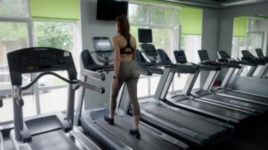 Bir kız sporcu koşu bandında adım atıyor. Bir kadın antrenmandan önce bacak kaslarını ısıtır. Spor malzemeleriyle hafif fiziksel aktivite. Kapatın. Yüksek kalite 4k görüntü