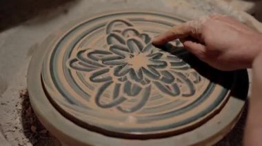 Kil tabağı yapıyorum. Dönen dairede boyama. Potter tek parmakla güzel sanat eserleri çiziyor. El yapımı Ukrayna geleneksel kültürel seramik imalatı. Ev atölyesi. Süsleri üzerine çiz