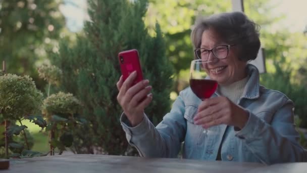 成熟的老年女性白发游客在视频通话中饮酒 并在餐厅平台上休息 一位有钱的老太太在户外咖啡馆录制视频博客时喝酒 高质量4K — 图库视频影像