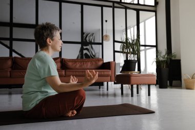 Orta yaşlı bir bayan evin büyük salonunda yoga yapıyor. Kapalı gözlü bir kadın nilüfer pozisyonundaki bir paspasın üzerinde yan yatar. Manevi gelişim kavramı
