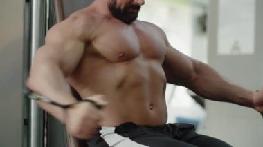 Spor salonundaki vücut geliştiren adam egzersiz makinesine kabloyla oturur. Sporcu esniyor, kollarını birleştiriyor ve ayırıyor. Göğüs kaslarını çalıştırmanın göstergesi. Yüksek kalite 4k görüntü