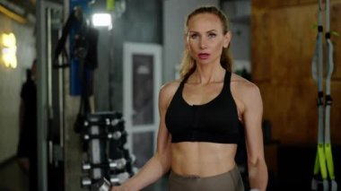 Spor salonunda kendine güveni olan genç bir atlet kız halterlerle egzersiz yapıyor. Nefes alıyor, kaldırıyor ve kollarını yanlara açıyor. Vücudun güzelliğini ve gücünü gösteriyor. Bir spor yaşam tarzı konsepti