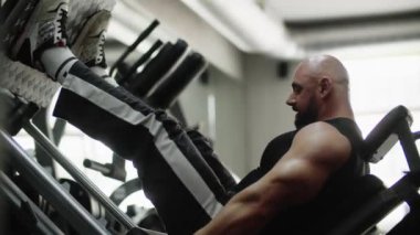 Vücut geliştiren adam spor salonunda makineye konsantre bir şekilde çalışıyor. Bacak dayanıklılığı ve dayanıklılık egzersizi. Sporcu bacaklarını yukarı ve aşağı eğip uzatır. Yüksek kalite 4k görüntü