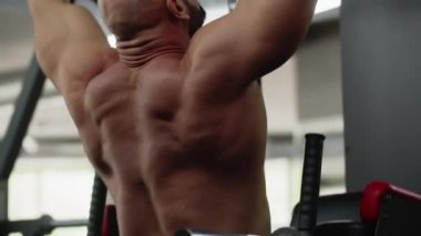 Delikanlı vücut geliştirici yatay barın oradaki spor salonunda barfiks çekiyor. Kolların, sırtın ve boynunun kaslarını çalıştırıyorum. Vücudun güzelliğini, gücünü, gücünü ve dayanıklılığını gösteriyor. Yüksek kalite