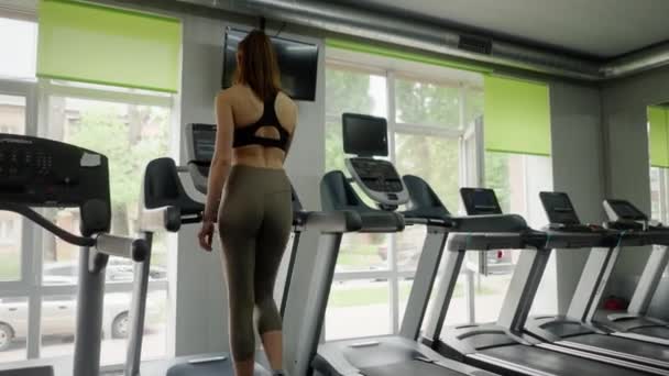 女の子アスリートがトレッドミルに乗る 女性はトレーニング前に脚の筋肉を温める スポーツ用具を使用した軽い身体活動 クローズアップ 高品質の4K映像 — ストック動画