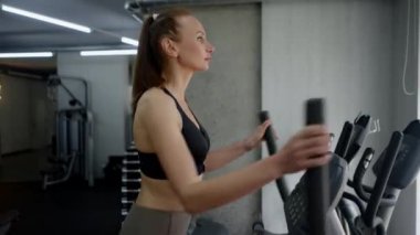 Mükemmel formda genç ve narin bir kadın spor salonuna girer ve bacak egzersizi makinesini özelleştirir. El hareketi ve pedal çevirme. Spor yaşam tarzı ve sağlıklı kavramı