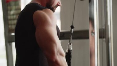 Spor salonundaki genç bir vücut geliştirme uzmanı kol kaslarını egzersiz makinesinde çalıştırıyor ve onların gücünü gösteriyor. Kolunu bir aşağı bir yukarı bükerek. Kabloları ağırlıkla kaldırıyorum. Bir erkek...