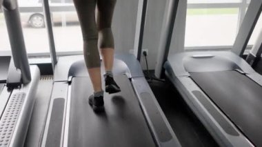 Bir kız sporcu koşu bandında adım atıyor. Bir kadın antrenmandan önce bacak kaslarını ısıtır. Spor malzemeleriyle hafif fiziksel aktivite. Kapatın. Yüksek kalite 4k görüntü