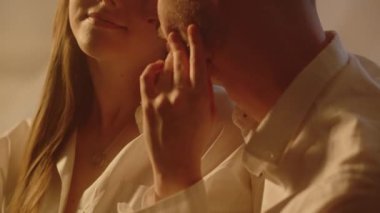 Kocasından zevk alan genç kız arkadaşı nazikçe boynunu ve şakaklarını öpüyor. Ev içinde aile fotoğrafı çekimi. Güzel bir kadın, öpüşen sevgilisinin yüzünü tatmin etmeyi sever. Yüksek kalite 4k görüntü