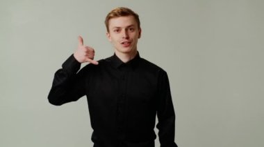 Siyah tişörtlü adam, gri arka planda izole edilmiş olduğunu söylüyor. Genç maço selamlama sinyali veriyor. Yarın beni ara. Mutlu adam flört ediyor ve telefon jesti yapıyor. Yüksek kalite 4k görüntü