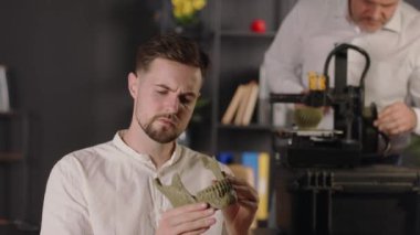 Genç bir araştırma asistanı el ele tutuşup insan çene kemiğinin haki renkli plastik modelini görüyor. Orta yaşlı bir makine mühendisi dijital kalibreler kullanır ve 3D yazıcının çalışmasını özelleştirir