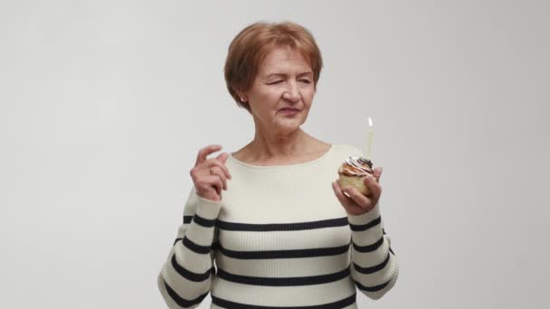 一位老妇人将彩饼放在掌心 作为圣诞节 新年或生日的礼物 举起手 闭上眼睛 头数到三 许个愿 吹灭蜡烛 尝一尝 — 图库视频影像