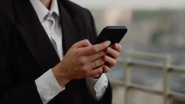 Şehrin merkezindeki büyük ofisin çatısındaki çekici genç iş kadınına yakın çekim. Dışarıdaki modern akıllı telefonu kullanarak ve mesaj yaz. Yüksek kalite 4k görüntü