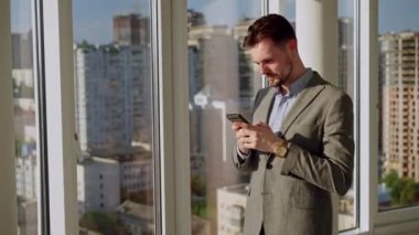 A successful young businessman in a nice suit in the office near the window picks up the phone and calls. The concept of happiness, success, and good emotions. High quality 4k footage