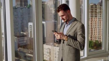 A successful young businessman in a nice suit in the office near the window picks up the phone and calls. The concept of happiness, success, and good emotions. High quality 4k footage