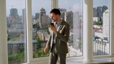 A successful young businessman in a nice suit in the office near the window picks up the phone and calls. The concept of happiness, success, and good emotions. High quality 4k footage