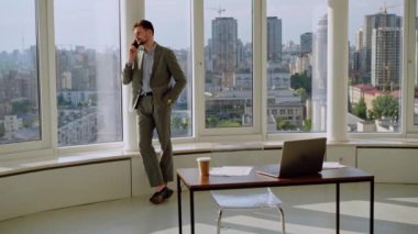 A successful young businessman in a nice suit in the office near the window picks up the phone and calls. The concept of happiness, success, and good emotions. High quality 4k footage