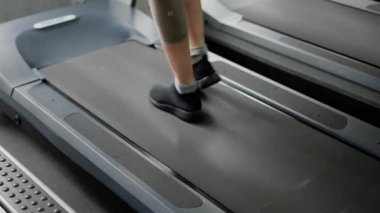 Bir kız sporcu koşu bandında adım atıyor. Bir kadın antrenmandan önce bacak kaslarını ısıtır. Spor malzemeleriyle hafif fiziksel aktivite. Kapatın. Yüksek kalite 4k görüntü