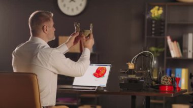 Grafik tasarımcısı insan çene kemiğinin plastik 3D baskılı modelini yandan tutuyor ve görüyor. Laptop ekranında kırmızı renkli bir kalp resmi. Protezler için biyobasım organları konsepti ve
