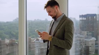 A successful young businessman in a nice suit in the office near the window picks up the phone and calls. The concept of happiness, success, and good emotions. High quality 4k footage