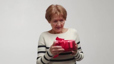 Yaşlı, güler yüzlü, neşeli bir kadın yakalar, ellerini tutar ve şaşkınlıkla sarılır parlak kırmızı bir hediye kutusuna kurdele ve fiyonk koyar. Hoş bir sürpriz duygusunun göstergesi. Şey...