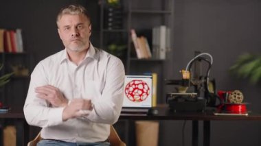 Pozitif gülümseyen orta yaşlı bir grafik tasarımcısı dizüstü bilgisayar kullanır ve geometrik katının üç boyutlu kırmızı modelini çizer. Otomatik özerk süreçte çalışan bir 3d yazıcı makinesi