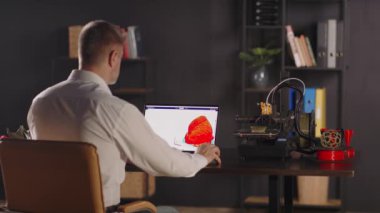 Grafik tasarımcı bir adam dizüstü bilgisayar kullanır, kırmızı ve sarı renkli vazo çizimi yapar ve geometrik formda bir vazo yapar. Bir 3D yazıcı otomatikleştirilmiş otonom işlemde çalışır. Konsept: