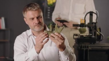 Orta yaşlı bir bilim adamı insan çene kemiğinin haki renkli plastik modelini tutuyor ve dişlerin gücünü kontrol ediyor. Genç bir araştırma asistanı 3D yazıcının çalışmalarını gözlemliyor, tablet kullanıyor ve...