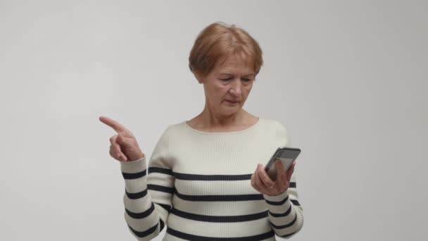 焦点を当てた視線を持つ高齢女性は スマートフォンを保持し 画面に触れ 波インデックス指を揺さぶります 否定的なサイン 顔に微笑みを浮かべた老婦人フォーフィンガーは別として — ストック動画