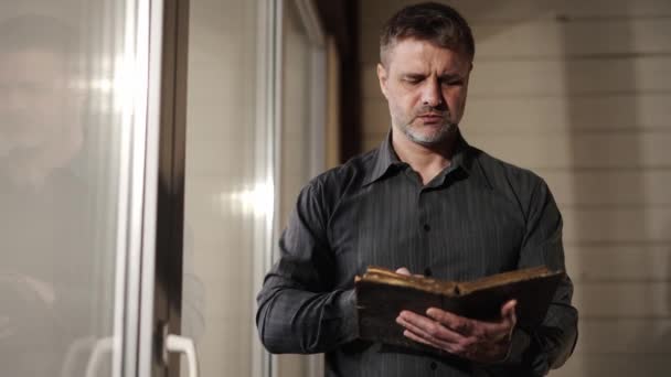 撃たれた聖書を閉じる 古文学を読んでいる男性の祈り 宗教的な聖書を保持している黒いシャツの男 救いへの希望 伝統的なスピリチュアルな聖書を探求する 高品質の写真 — ストック動画