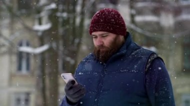 Yetişkin sakallı bir adam dışarıda akıllı telefon kullanarak kırmızı şapka takıyor. Mesajda 