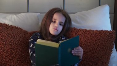 Yatmadan önce kitap okuyan küçük bir kız. Uykulu Protestan din kızı İncil okuyor. Dini aile kavramı. Din edebiyatı öğrenen küçük bir kız. Uyumadan önce eğitim. Yüksek
