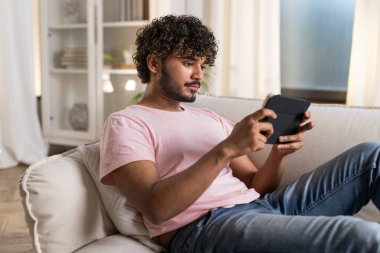 Odadaki kanepede uzanmış gülümseyen mestizolu bir adam işten sonra dinlenmeyi ya da rahat ev ortamında ders çalışmayı sever. Pozitif bir Afrikalı ya da Amerikalı bir adam elinde bir tablet tutarak...