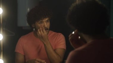 Çekici bir afro-amerikan erkek aktör ya da manken küpe takar, soyunma odasında aynanın önüne geçer, sünger kullanarak pudrayı yüzüne sürer, sahne veya profesyonel sahne için hazırlanır.