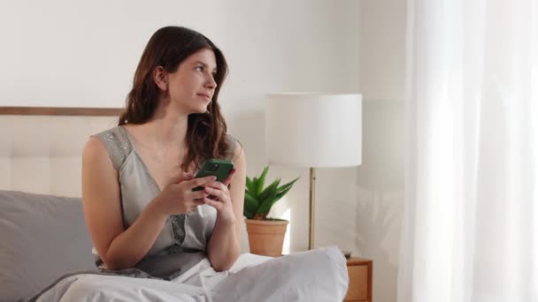 Uma Jovem Atraente Senta Uma Cama Com Telefone Nas Mãos — Vídeo de Stock