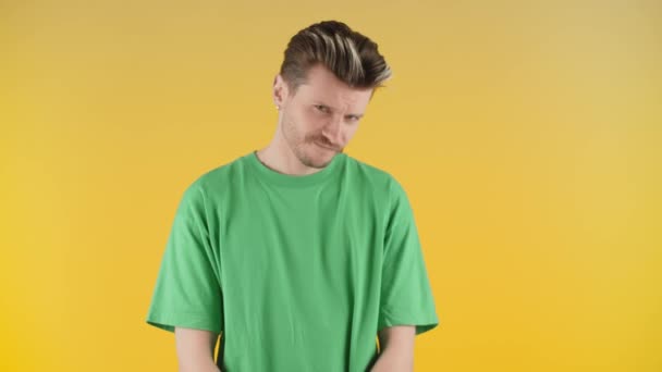 黄色の背景にカメラのための頑固なポーズを持つ若い男 緑色のTシャツを着た男が頭を下げてカメラを見ている 高品質4K映像 — ストック動画