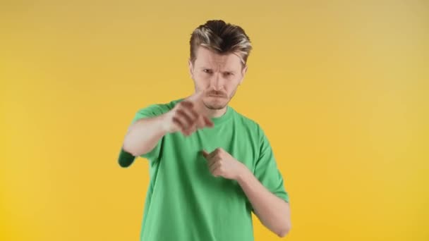 緑のTシャツの男が手をパンチし カメラを指しています 積極的な若い男が黄色の壁の背景に立っている 高品質4K映像 — ストック動画