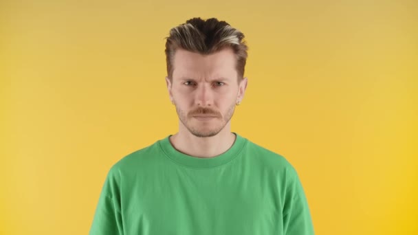 屈強な青年が黄色い壁に立ち カメラをじっと見つめた 緑のTシャツを着た眉をひそめる男がカメラをポーズ 高品質4K映像 — ストック動画