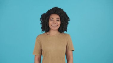 Çekici Afrikalı Amerikalı bir kadının mavi arka planda kameraya gülümseyişi ön planda. Güzel siyah kız mutluluğunu ifade ediyor. Yüksek kalite 4k görüntü