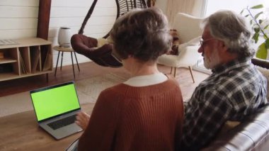 Dizüstü bilgisayar kullanan gri saçlı emekliler kanepede otururlar. Evde dizüstü bilgisayar kullanan yaşlı çift. Yüksek kalite 4k görüntü