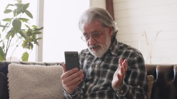 老年人在视频通话时看着手机屏幕 祖父戴着眼镜 穿着格子衬衫 在电话里聊天 高质量的4K镜头 — 图库视频影像