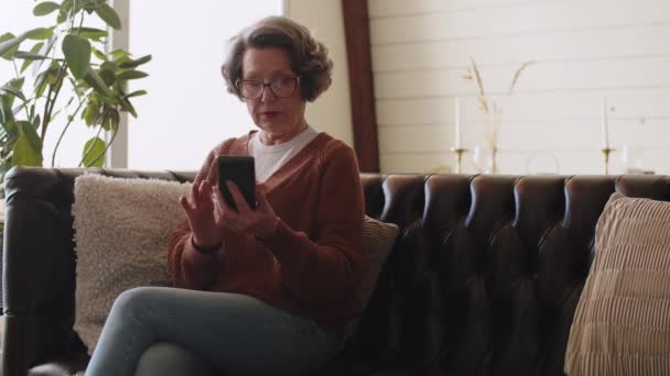 Зрелая Женщина Пользующаяся Телефоном Сидящая Диване Просматривающая Приложения Смартфонов Глядящая — стоковое видео