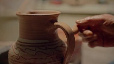 Potter atölyede el yapımı kil testisini bitiriyor. Yakın çekim zanaatkar parmakları tencere sapına ıslak ekleyerek. Çalışkan çömlekçi, kâse çizimleri için son detayları yapıyor. Seramik kap. Yüksek
