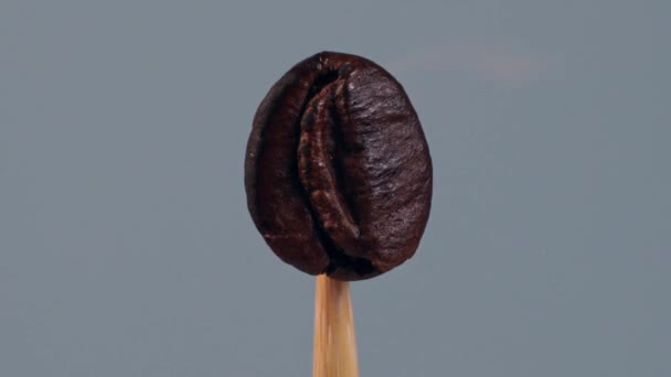 点火した茶色のコーヒー豆は 木製の棒に置かれ 灰色の背景に隔離され 炎の中で揚げられ 火の影響下に落ちます クローズアップ スローモーションモード — ストック動画